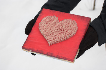 panels of thread and nails, heart on a red background. string art on a white background in the hands. gift or decoration for February 14 and March 8. with love
