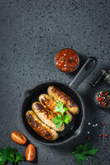 Fried spicy  sausages in cast iron skillet on dark background. Top view, space for text.