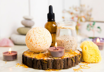 Side view of home wellness spa products, orange bath bomb, aroma bath salt, sea sponge, tea candles...