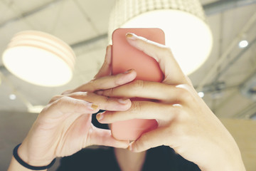 Close up of women's hands with a pink nails holding cell telephone, hipster girl watching video and...