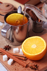 Preparing of black tea in metallic cup with orange fruit and cinnamon sticks