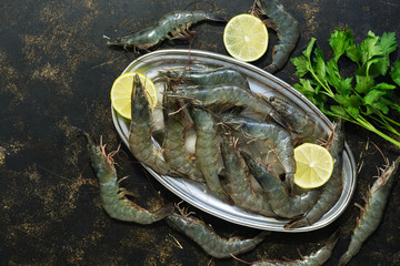 Fresh raw tiger shrimps on a metal plate with ice, lemon and parsley on a dark background. Top...