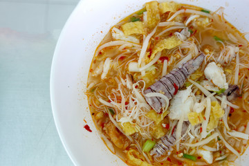 Spicy seafood noodles soup with crayfish, shrimp and mushroom. Asia food in white bowl on table background. Thai style noodle and street food of Thailand.