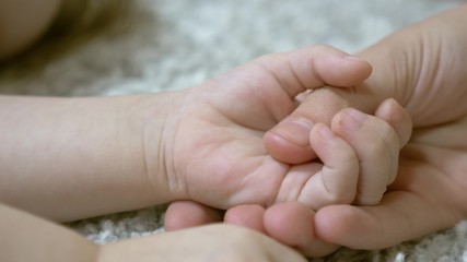 Mom is holding hand of little baby. Maternal care for small child. Close-up.