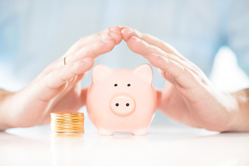 Saving money. Accounting, business, budget and finance concept. Male hands above piggy bank near coins stack.