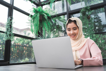 Beautiful young smiling asian muslim woman working on laptop sitting in living room at home. Asian business woman working document finance and calculator in her home office. Enjoying time at home.