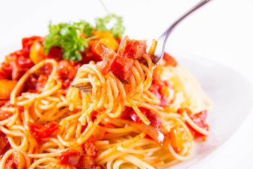 Spaghetti with sauce decorated with parsley eaten with a fork on a white background