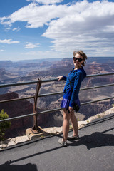 Female tourist stands close to the edge railing at an overlook at Grand Canyon National Park in Arizona