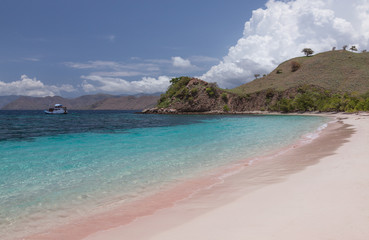 Fototapeta na wymiar Pink beach with crystal clear water and a boat near tropical islands