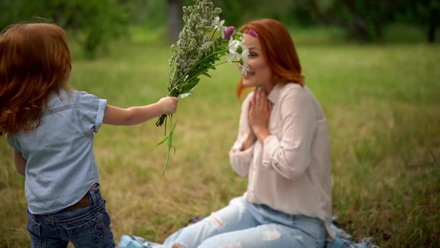 Beautiful kid gives flowers to smiling mother