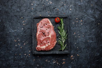 Food background. Raw rib eye steak with tomatoes and rosemary on black background top view.