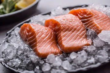 Portioned raw salmon fillets in ice on plate with lemon and rosemary