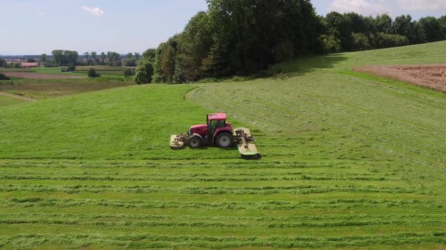 Aerial view of a tractor mowing a green fresh grass field on a sunny day.