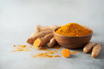 Turmeric powder in wooden bowl and fresh turmeric root on grey concrete background. Banner with copy space - obrazy, fototapety, plakaty