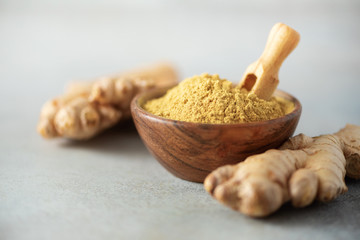 Ginger root and ginger powder in wooden bowl over grey concrete background with copy space. Immune...