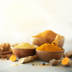 Ingredients for hot ayurvedic drink. Turmeric powder, curcuma root, cinnamon, ginger, lemon over grey background. Copy space, square crop. Spices for alternative medicine
