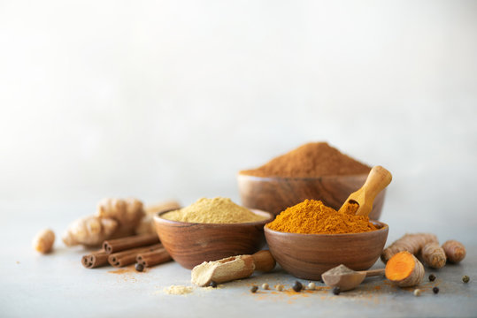 Ingredients for turmeric latte. Ground turmeric, curcuma root, cinnamon, ginger, black pepper on grey background. Spices for ayurvedic treatment. Alternative medicine concept