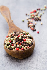 Peppercorn mix in a wooden bowl on grey table.