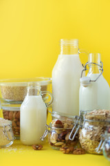 Vegan substitute dairy milk. Glass bottles with non-dairy milk and ingredients over yellow background with copy space. Clean eating, dairy-free, vegan, allergy-friendly, healthy food concept