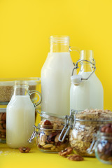 Glass bottles of vegan plant milk and almonds, nuts, coconut, hemp seed milk on yellow background. Banner with copy space. Dairy free milk substitute drinks and ingredients