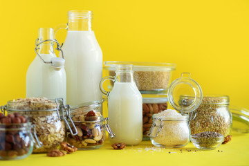 Glass bottles of vegan plant milk and almonds, nuts, coconut, hemp seed milk on yellow background. Banner with copy space. Dairy free milk substitute drinks and ingredients