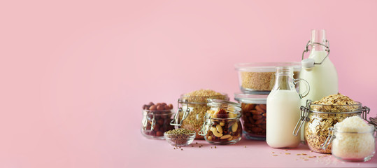 Glass bottles of vegan plant milk and almonds, nuts, coconut, hemp seed milk on pink background....
