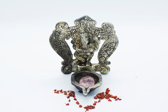 An ornate statue of ganesh / ganesha statue holding a rose quartz, surrounded by red chakra stones on an isolated white background