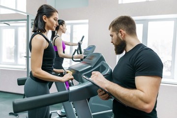 Fototapeta na wymiar Young smiling fitness women with personal trainer an adult athletic man on treadmill in the gym. Sport, teamwork, training, healthy lifestyle concept