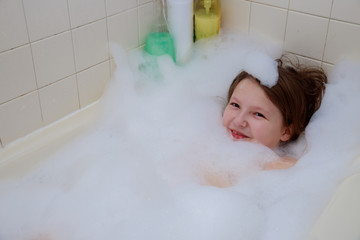 Happy baby in the bath, swimming in the foam shower.