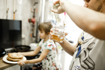 Father pours honey in the bowl and his little daughter takes a plate with pancakes in the kitchen