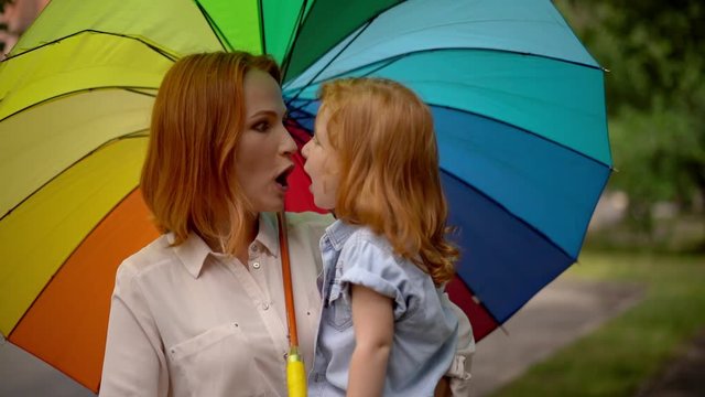 Mom and girl under colored umbrella in nature