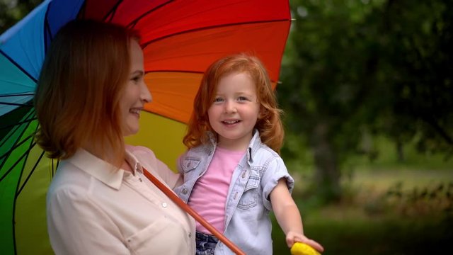 Mom and girl under colored umbrella in nature
