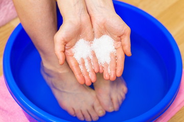 Woman using salt for feet in foot bath - obrazy, fototapety, plakaty
