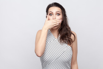 I will be silence. Portrait of shocked beautiful young brunette woman with makeup and striped dress...