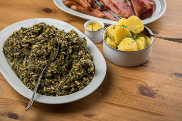 Oldenburger Grünkohl, Kassler Nacken, Kohlwurst und Pinkel auf Platten mit Kartoffeln und Senf auf Holz Tisch