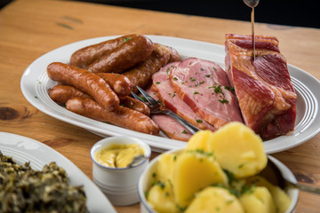 Kassler Nacken, Kohlwurst, Pinkel und Oldenburger Grünkohl auf Platten mit Kartoffeln und Senf auf Holz Tisch