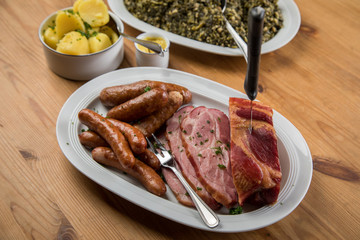 Kassler Nacken, Kohlwurst, Pinkel und Oldenburger Grünkohl auf Platten mit Kartoffeln und Senf auf Holz Tisch