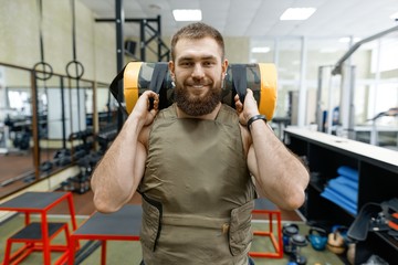 Portrait muscular caucasian bearded man dressed in weighted vest in the gym, military style
