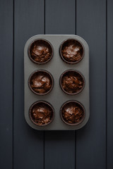 Batter for homemade chocolate muffins in baking tray on dark background top view