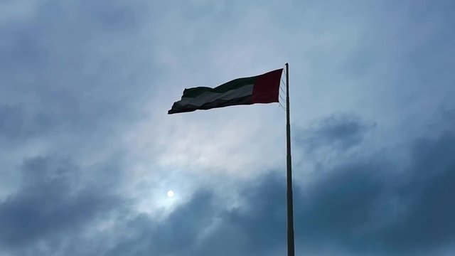 The United Arab Emirates flags waving in Abu Dhabi city - clouds and sun light