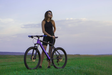 Fototapeta premium A girl riding a mountain bike on an asphalt road, beautiful portrait of a cyclist at sunset 