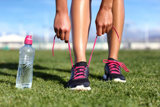 Start training healthy active lifestyle concept- Runner girl getting ready to exercise on grass tying running shoes with water bottle.
