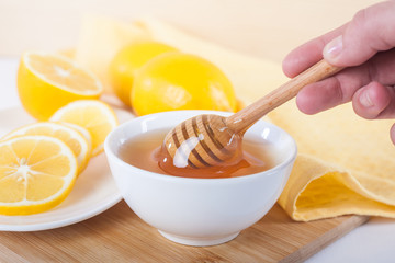 honey in a white ceramic bowl with honey dipper and lemon on a wooden kitchen boar