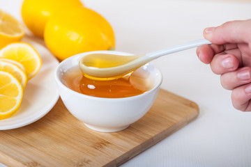 honey in a white ceramic bowl with spoon and lemon on a wooden kitchen board