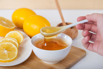 honey in a white ceramic bowl with spoon and lemon on a wooden kitchen board