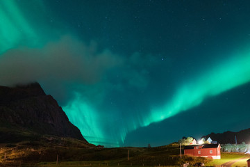 Fototapeta na wymiar Northern lights Aurora Borealis over illuminated fishing village of reine lofoten islands.