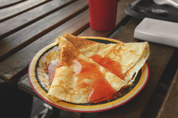 Delicious pancakes with jam on a disposable plate on a wooden table in a cafe