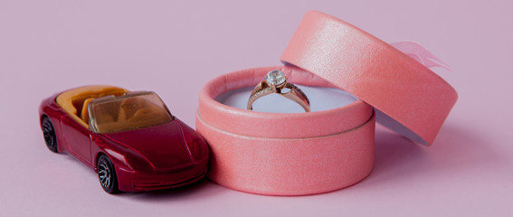 Toy car with wedding ring box on pink background