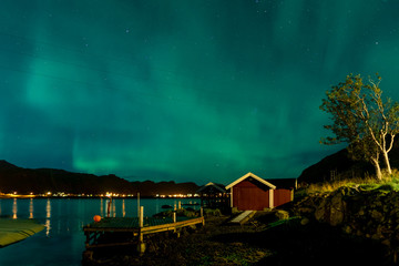 Northern lights Aurora Borealis over illuminated fishing village of reine lofoten islands.
