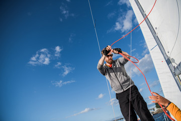 Handsome bearded sailor working with ropes on deck of a yacht against clear blue sky and sea